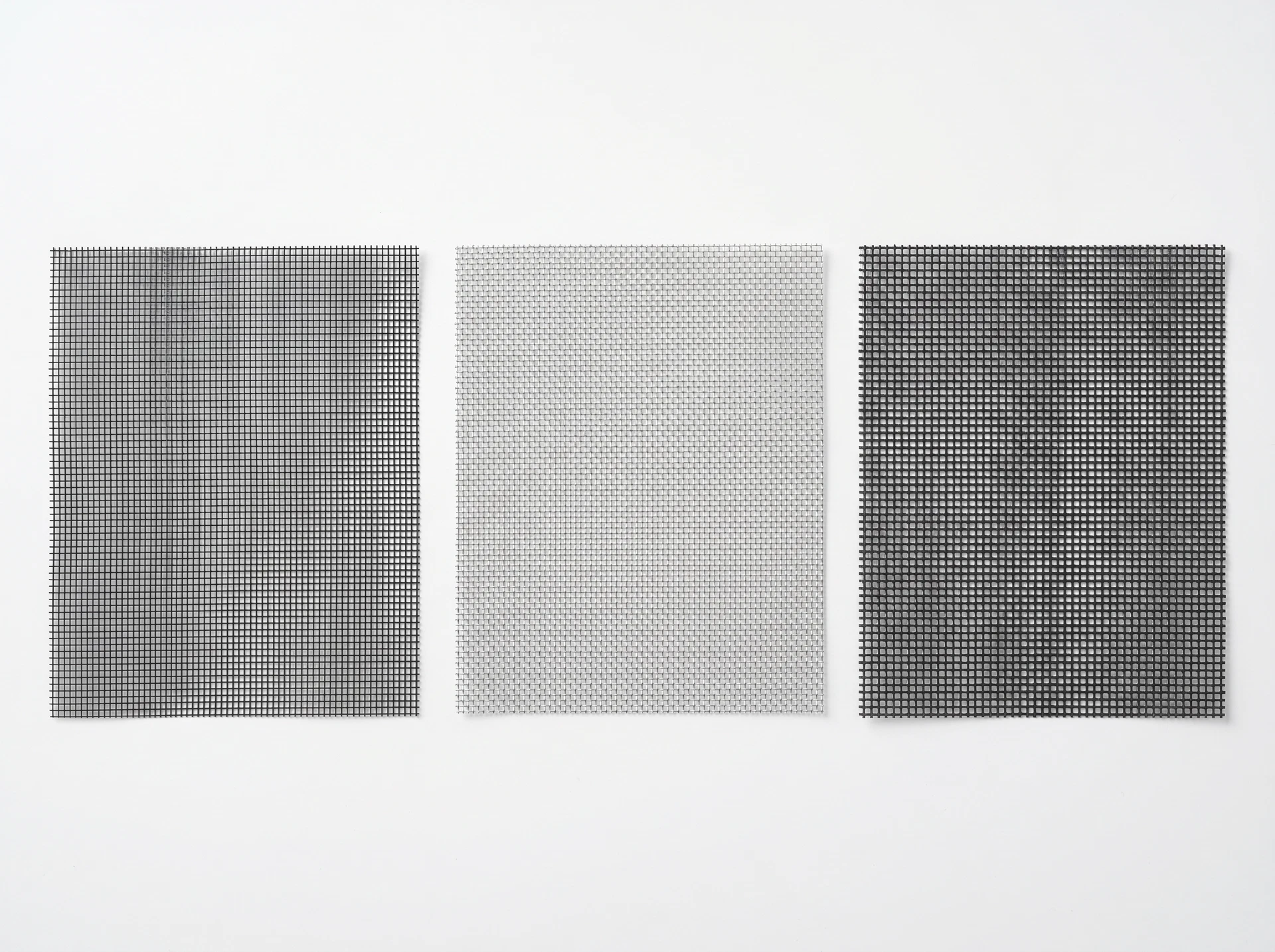 Three window screen mesh samples side by side: standard charcoal fiberglass, silver aluminum, and dark pet-resistant polyester mesh